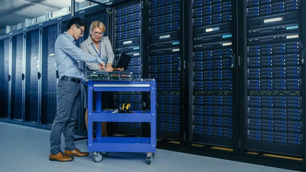 W nowoczesnym centrum danych: inżynier i Specjalista IT pracują ze stojaków serwerowych, na sprzęcie Pushcart do instalacji nowego sprzętu. Specjaliści zajmujący się konserwacją i diagnostyką bazy danych. — Zdjęcie stockowe