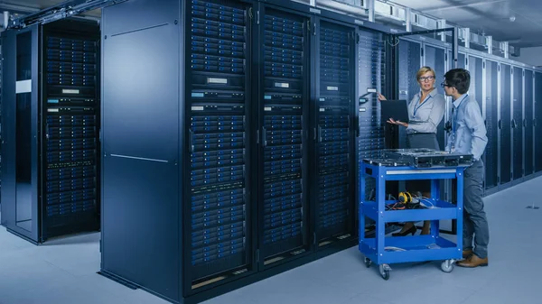 Im modernen Rechenzentrum: Ingenieur und IT-Spezialist arbeiten mit Serverschränken, an einer Schubkarren-Ausrüstung für die Installation neuer Hardware. Spezialisten für Wartung und Diagnose der Datenbank. — Stockfoto