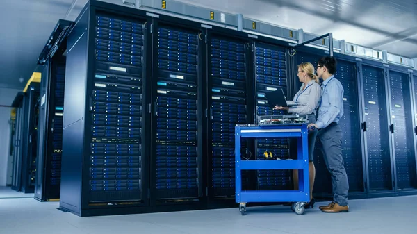 No Data Center Moderno: Engenheiro e Especialista em TI Trabalhe com Racks de Servidor, em um Equipamento Pushcart para Instalação de Novos Hardware. Especialistas Fazendo Manutenção do Banco de Dados. Tiro de ângulo baixo . — Fotografia de Stock