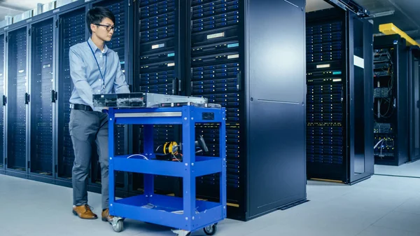 No Data Center Moderno: Técnico de TI Trabalhando com Racks de Servidor, Empurra Carrinho Entre Linhas de Racks de Servidor. Em um novo hardware Pushcart para atualização do sistema. Engenheiro fazendo manutenção e diagnósticos . — Fotografia de Stock