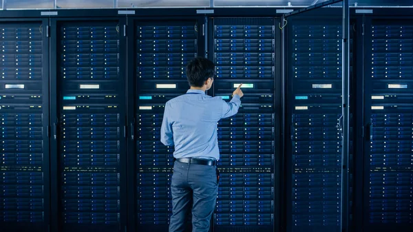 In the Modern Data Center: IT Engineer Standing Beside Open Server Rack Cabinets, Does Wireless Maintenance and Diagnostics Procedure with a Laptop. He Touches Server Buttons. — Stock Photo, Image