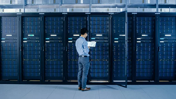 En el centro de datos moderno: Ingeniero de TI junto a gabinetes de bastidor de servidor abierto, hace el mantenimiento inalámbrico y el procedimiento de diagnóstico con un ordenador portátil . —  Fotos de Stock