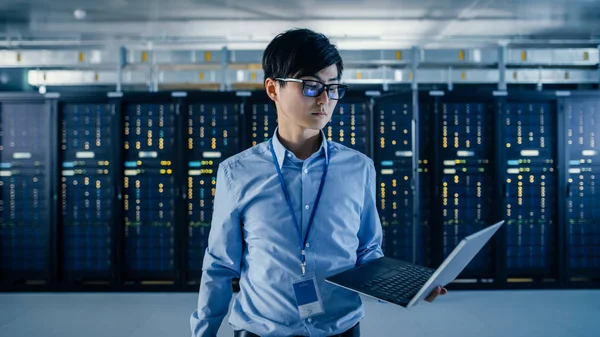 In the Modern Data Center: Portrait of IT Engineer Standing with Server Racks Behind Him, Holding Laptop and Looking at the Camera. Finishing Doing Maintenance and Diagnostics Procedure. — Stock Photo, Image