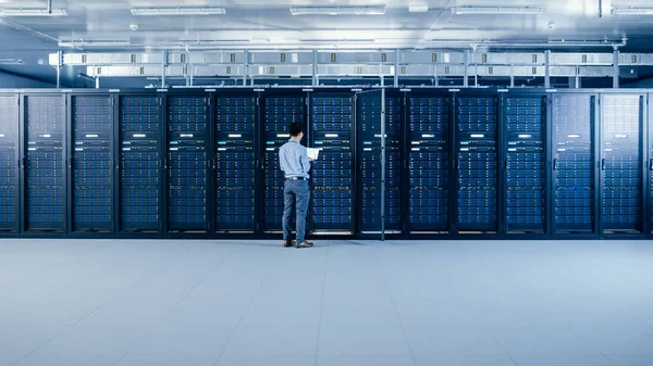 En el centro de datos moderno: Ingeniero de TI junto a gabinetes de bastidor de servidor abierto, hace el mantenimiento inalámbrico y el procedimiento de diagnóstico con un ordenador portátil . — Foto de Stock