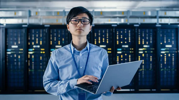 In the Modern Data Center: Portrait of IT Engineer Standing with Server Racks Behind Him, Holding Laptop and Looking at the Camera (en inglés). Acabado Mantenimiento y Diagnóstico Procedimiento . —  Fotos de Stock