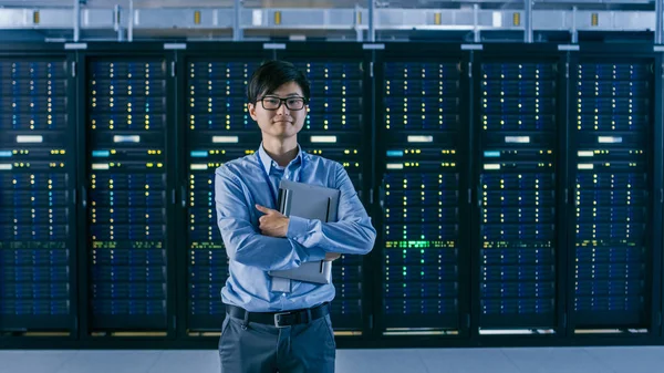 In het moderne Data Center: portret van IT-ingenieur staande met server racks achter hem, het houden van laptop na het beëindigen van onderhoud en diagnostiek procedure. — Stockfoto