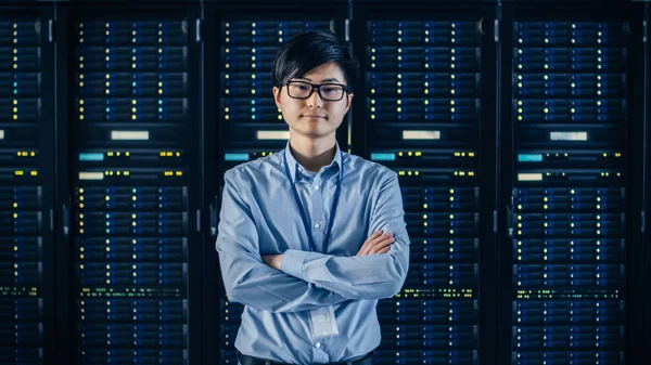 In the Modern Data Center: Portrait of IT Engineer Standing with Server Racks Behind Him, Crossing Arms (en inglés). Especialista en TI profesional que trabaja en un centro de datos moderno con tecnologías innovadoras . —  Fotos de Stock
