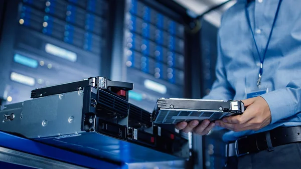 Dalam Pusat Data Modern: IT Engineer adalah Holding New HDD Hard Drive Prepared untuk Installing Hardware Equipment into Server Rack. Spesialis IT Melakukan Pemeliharaan dan Pemutakhiran Perangkat Keras . — Stok Foto