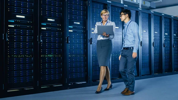 Nel moderno data center: Ingegnere e specialista IT lavora con server rack, parla, fa la manutenzione del sistema di controllo con computer portatile. Specialisti in diagnostica del database . — Foto Stock