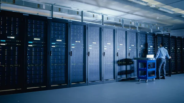 In the Modern Data Center: IT Engineer Doing Maintenance and Diagnostics. Empuja el carro junto con los bastidores del servidor, abre el gabinete para instalar nuevo hardware para la actualización del sistema planificado, reemplazo del equipo . — Foto de Stock