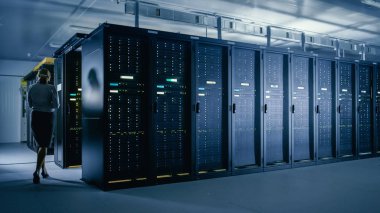 Veri merkezi 'nde: kadın BT teknisyeni sunucu rafları satır yanında yürür, böylece Mainframe optimum Işlev düzeyinde çalışır bakım tanılama çalıştırmak için dizüstü bilgisayar kullanır.