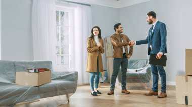 Profesyonel gayrimenkul ajanı genç çift Bright yeni daire gösterir. Başarılı genç çift ev sahibi olma, el sıkışması ile gayrimenkul broker ile anlaşma Seal. Büyük pencereler ile Bright Home