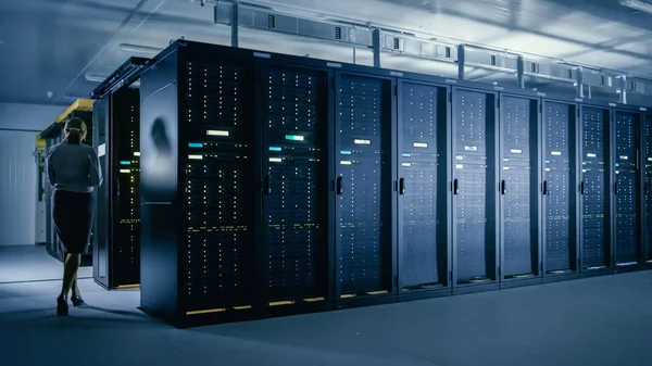 Veri merkezi 'nde: kadın BT teknisyeni sunucu rafları satır yanında yürür, böylece Mainframe optimum Işlev düzeyinde çalışır bakım tanılama çalıştırmak için dizüstü bilgisayar kullanır.