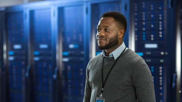 Black Data Center IT-technicus staat in het midden van een server rack corridor. Hij glimlacht. — Stockfoto