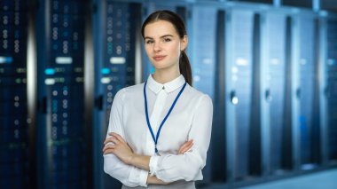 Female It Specialist, sunucu rafları ve kameraya bakarak veri merkezinde kamera 'da duruyor. Onun Arms çapraz ve o kamera Smiles.