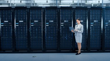 Kadın veri merkezi BT mühendisi dizüstü bilgisayar sunucu raf koridor yanında çalışır. Tanılama çalıştırma veya bakım çalışması yapma.