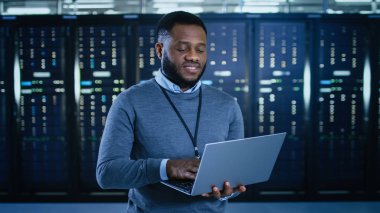 Siyah veri merkezi o teknisyen bir dizüstü bilgisayar ile bir sunucu raf koridor ortasında ayakta. O çalışma sunucu dolapları görsel teftiş olduğunu.