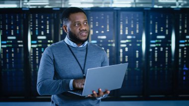 Siyah veri merkezi o teknisyen bir dizüstü bilgisayar ile bir sunucu raf koridor ortasında ayakta. O çalışma sunucu dolapları görsel teftiş olduğunu.