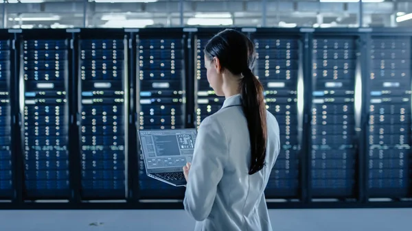 Zadní záběr ženského datového centra IT specialista pracuje na přenosném počítači vedle regálu na serveru. Spuštění diagnostiky nebo práce v údržbě. — Stock fotografie