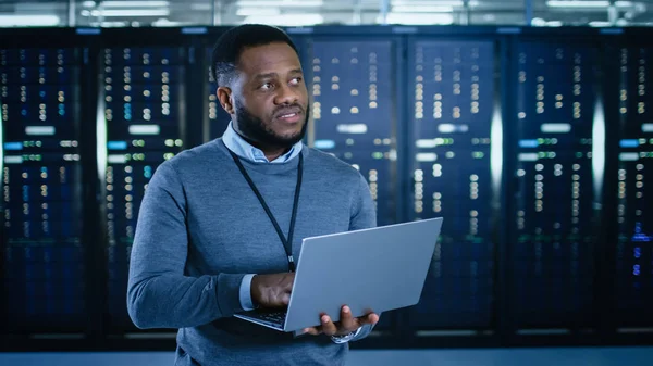 Siyah veri merkezi o teknisyen bir dizüstü bilgisayar ile bir sunucu raf koridor ortasında ayakta. O çalışma sunucu dolapları görsel teftiş olduğunu.