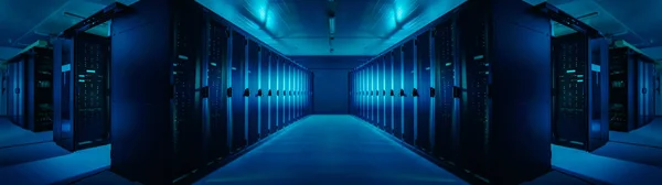 Širokoúhlé panoráma pracovního datového centra s řádky rozvaděčového serveru. Modré indikátory LED blikají a počítače fungují. Tmavé okolní světlo. — Stock fotografie