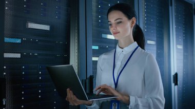 Emin ve güzel kadın It Engineer sunucu raf önce ayakta iken veri merkezinde laptop üzerinde çalışıyor. Tanılama çalıştırma veya bakım çalışması yapma.