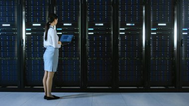 Güzel veri merkezi kadın o teknisyen bir dizüstü bilgisayar ile sunucu raf koridoru üzerinden yürüyüş. O durur ve görsel sunucu dolapları çalışma Inceler.