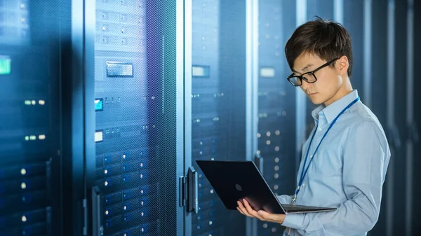 In the Modern Data Center: IT Engineer Standing Beside Server Rack Cabinets, Does Wireless Maintenance and Diagnostics Procedure with a Laptop. — Stock Photo, Image