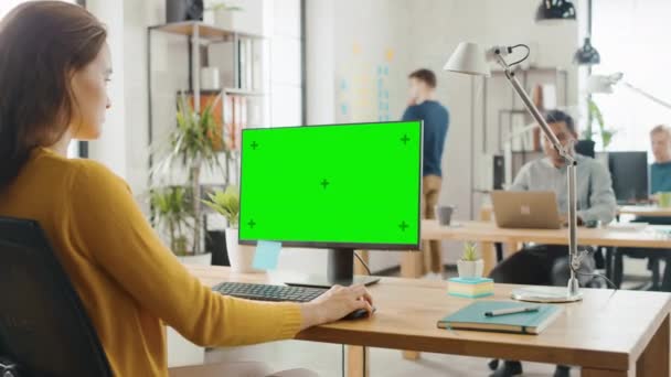 Над плечом: творческая молодая женщина, сидящая за рабочим столом с макетом зеленого экрана. Брайт-офис, где разношерстная команда молодых ученых работает над компьютерами — стоковое видео