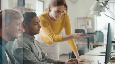 Yetenekli girişimci onun masaüstü bilgisayar üzerinde Proje Yöneticisi ile çalışma ve takım lideri onun yanında ayakta, tartışma var, sorun çözüm bulma. Ofiste çalışan parlak Insanlar