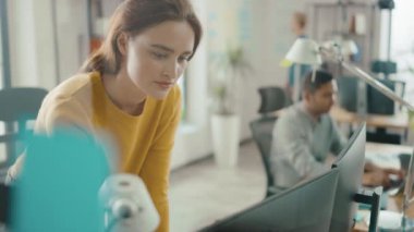 Güzel ve yaratıcı genç kadın oturma onu masa kullanarak laptop bilgisayar. Arka plan parlak ofiste genç profesyoneller çeşitli takım çalışma