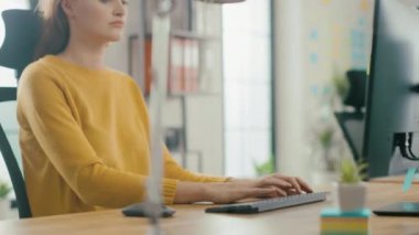 Güzel ve yaratıcı genç kadın portresi dizüstü bilgisayar kullanarak onun masasında oturan. Arka plan parlak ofiste genç profesyoneller çeşitli takım çalışma