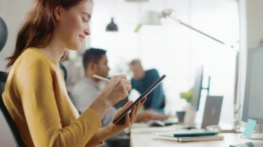 Yetenekli kadın Tasarımcısı masasında oturan o çizim, yazma ve dijital tablet bilgisayar ile kalem kullanma. Kalem ile Hands odaklanın. Genç profesyonellerin çeşitli ekibi çalışma parlak ofis