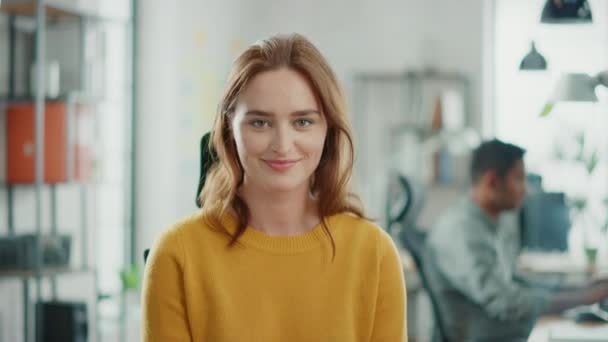 Portrait de belle jeune femme aux cheveux rouges portant un pull jaune souriant à la caméra avec charme. Une femme prospère qui travaille dans un bureau lumineux et diversifié — Video