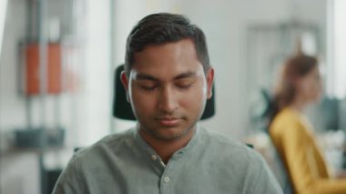 Onun masasında çalışan yakışıklı profesyonel Hint adam portresi, kişisel bilgisayar kullanarak ve kamera gülümsüyor. Parlak farklı ofiste çalışan başarılı adam