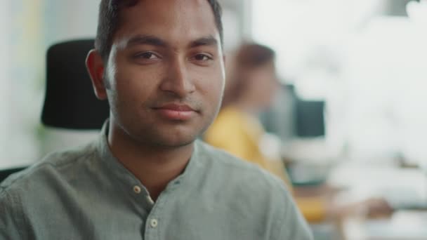 Retrato de un guapo indio profesional trabajando en su escritorio, mirando a la cámara. El hombre exitoso que trabaja en la oficina diversa brillante — Vídeo de stock