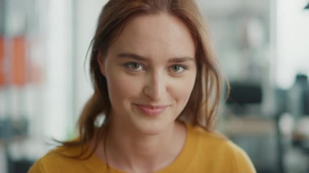 Porträtt av vacker ung kvinna med rött hår klädd gul Tröja tittar upp till kameran och leende charmigt. Framgångsrik kvinna som arbetar i ljusa olika kontor — Stockvideo