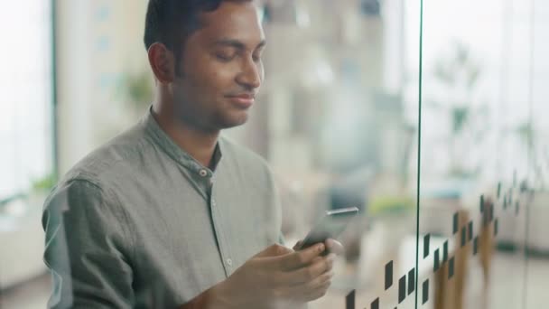 Retrato de guapo profesional indio utiliza el teléfono móvil, escribe correo electrónico importante. Hombre exitoso usando Smartphone Trabajando en Bright Diverse Office — Vídeo de stock