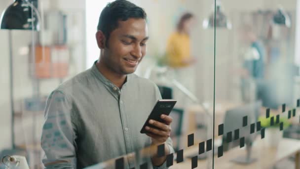 Portret przystojnego profesjonalnego indyjskiego człowieka używa telefonu komórkowego, pisze ważne email, uśmiechy charmingly, wraca do swojego miejsca pracy. Udany człowiek korzystanie Smartphone praca w różnorodnym biurze — Wideo stockowe