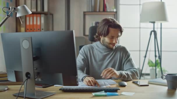 Schöner langhaariger Unternehmer, der an seinem Schreibtisch im Büro sitzt, arbeitet am Desktop-Computer, arbeitet mit Dokumenten, korrigiert Diagramme, zeichnet Diagramme — Stockvideo