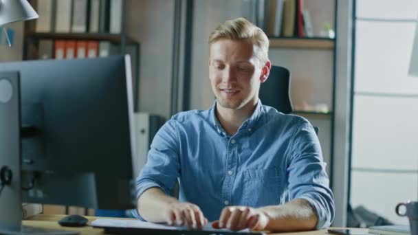 Handsome Blonde Entrepreneur Sentado en su escritorio en la oficina funciona en la computadora de escritorio, trabajando con documentos, gráficos, estadísticas y estrategia. Empresario creativo usando computadora — Vídeos de Stock