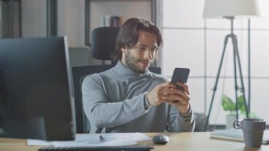 Yakışıklı Uzun Saçlı Girişimci Ofis 'teki Masasında Masaüstü Bilgisayarında, Belgeler ve Grafiklerle Çalışıyor. Akıllı Telefon, Sosyal Medya Uygulaması, E- posta Yazma, Mesajlaşma