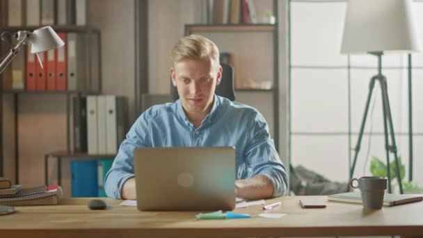 Snygg blond affärsman sitter vid sitt skrivbord i kontoret fungerar på en bärbar dator. Kreativ entreprenör med hjälp av dator som arbetar med programvara Unicorn Startup Project. Studentuppsats för universitetet — Stockvideo