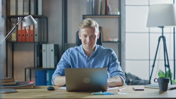 Snygg blond affärsman sitter vid sitt skrivbord i kontoret fungerar på en bärbar dator. Kreativ entreprenör med hjälp av dator som arbetar med programvara Unicorn Startup Project. Studentuppsats för universitetet — Stockvideo