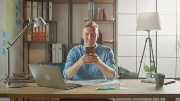 Kreativ entreprenör Sitter vid sitt skrivbord Fungerar på en bärbar dator i den eleganta Office, Använder Smartphone för sociala medier Apps, E-post Business Associates, Läsnyheter, Bläddra via Internet — Stockvideo