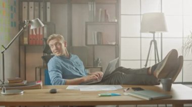 Yakışıklı Genç Girişimci Bacakları Masanın Üzerinde Dizüstü bilgisayarla Çalışıyor. Tasarımcı, Yazılım Unicorn Startup 'ı yaratmak için Not Defteri kullanır. Üniversite için Serin Öğrenci Yazma Kağıtları