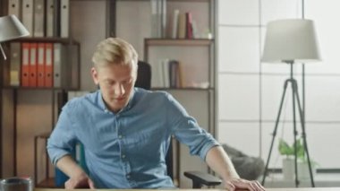 Yakışıklı Genç Girişimci Ofisine Giriyor Ve Masa Başında Laptop Uaçıyor ve Proje Üzerinde Çalışmaya Başlıyor. İşadamı Notebook Kullanma, E-posta Yazma, İnternet'te Gezinme, Başlangıç Yazılımı Tasarlama