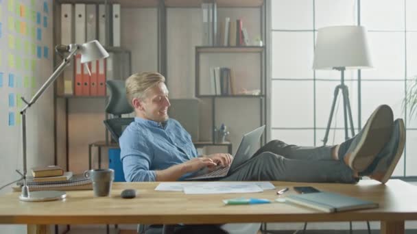 Успешный молодой предприниматель работает на ноутбуке с поднятыми ногами на столе. Дизайнер использует ноутбук для создания запуска программного обеспечения единорога. Письменная книга для студентов — стоковое видео