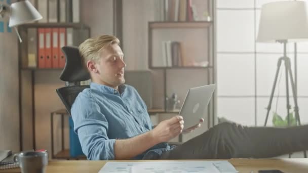 Handsome Young Entrepreneur Works on a Laptop with His Legs Up on the Desk. Designer Uses Notebook to Create Software Unicorn Startup. Chill Student Writing Paper for University — Stock Video