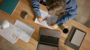 Ofiste Masasında Oturan İşadamı Dizüstü Bilgisayar Kullanır, Şirket Strateji Belgeleri ile Çalışır, Grafikleri Düzeltir, Grafik ve İstatistikleri Çizer. Üstten Görünüm Uzaklaştırma Döndürme Çekimi